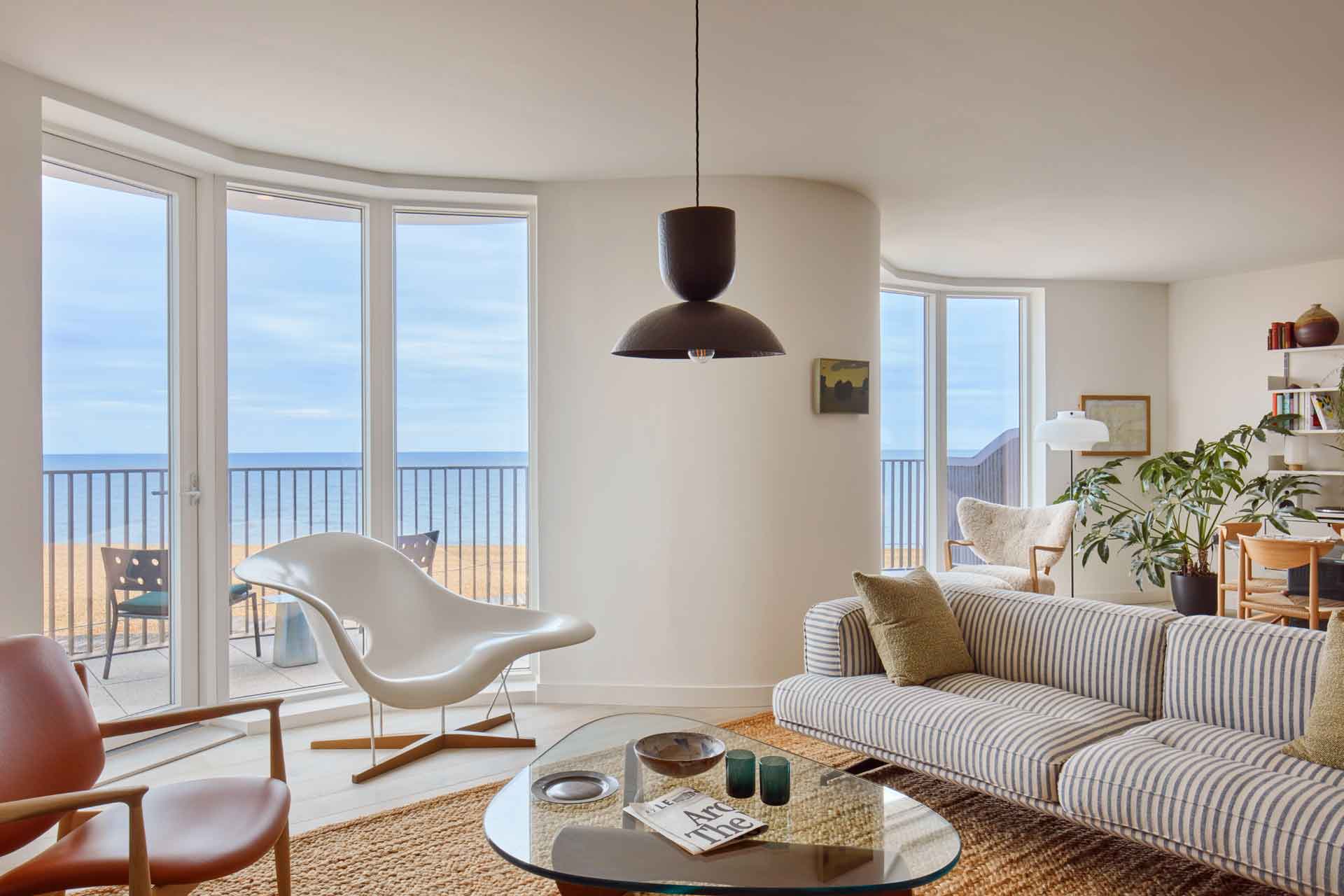 Curved living room with wooden flooring. cream furniture and floor-to-ceiling windows framing coastal views.