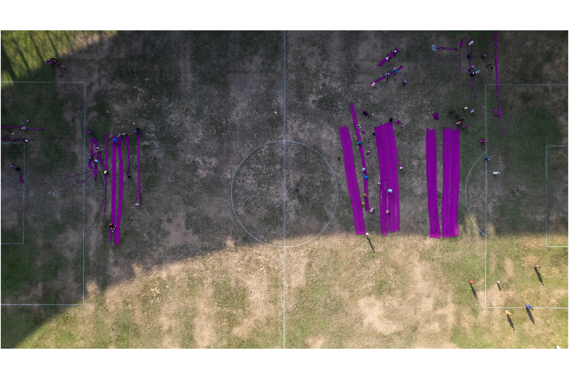 People stitching reams of purple fabric, seen from above