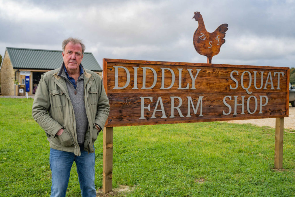 Jeremy Clarkson standing next to a sign for Diddly Squat Farm Shop