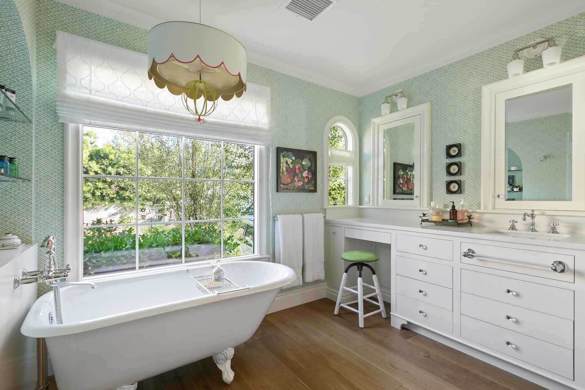 Large bathroom with rolltop bath, white cabinets and green patterned wallpaper.