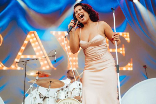 RAYE wearing a blush pink silk dress onstage at Forwards Festival