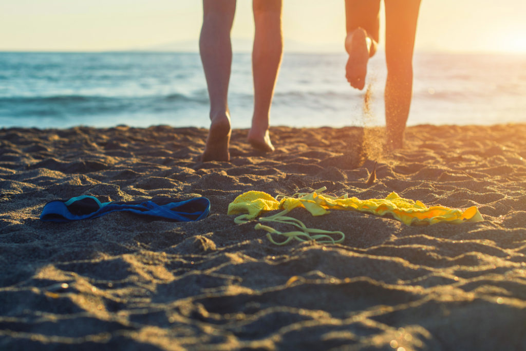 Female and male legs with bikini and swimming trunks on the beach on a sunset background
