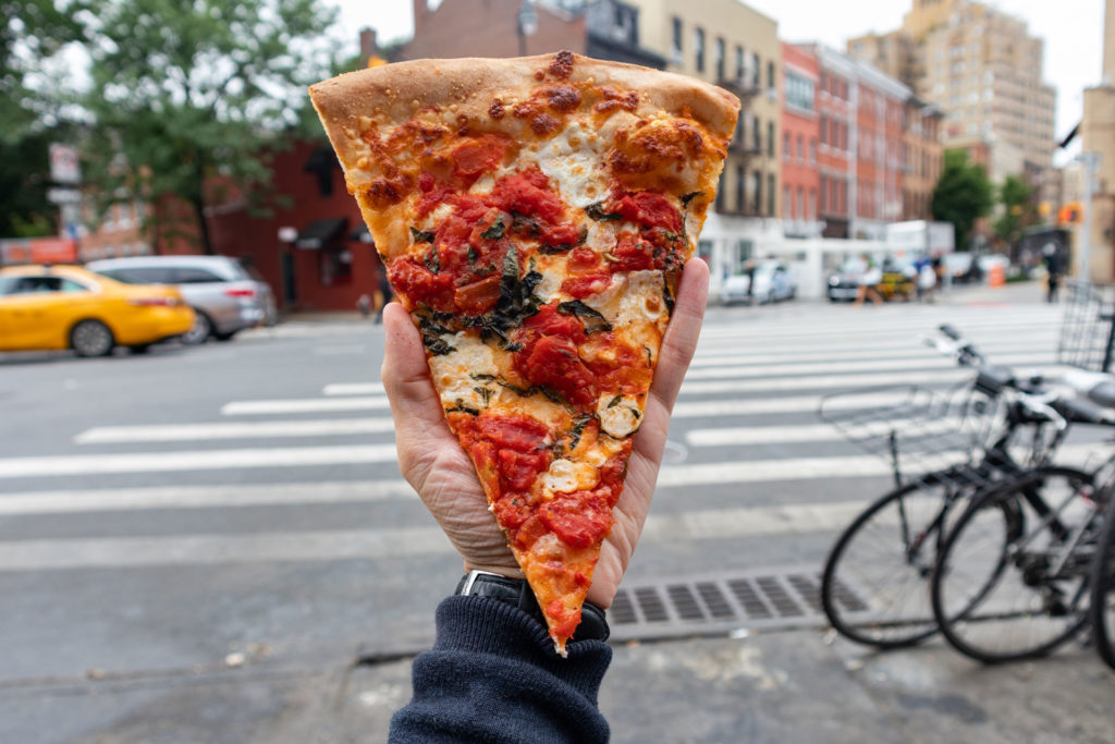 A hand holding a slice of pizza in New York
