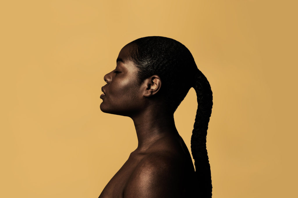 Black woman with hair tied back on yellow background | scalp health