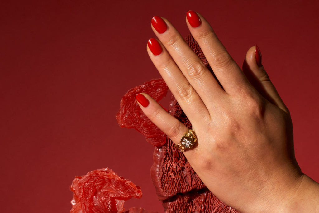 Hand with gold ring and red nails on red background