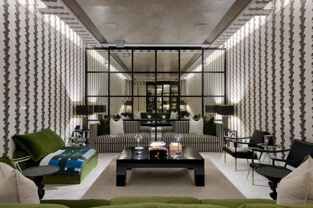 Living room with brown and white striped wallpaper, a Crittsall mirror and green sofas