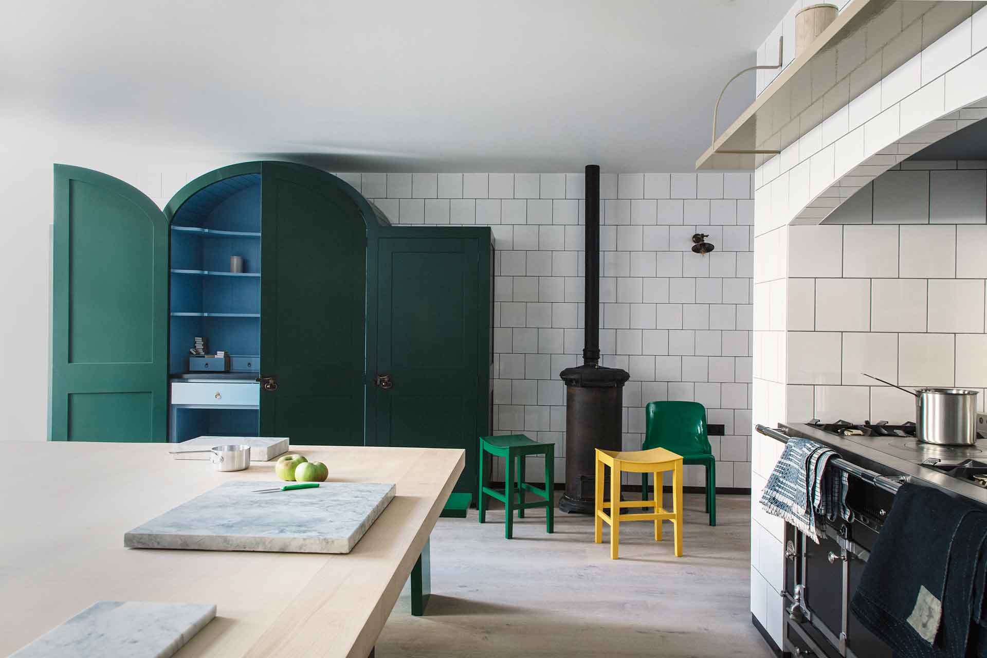 White-tiled kitchen with black AGA and curved blue freestanding cabinet.