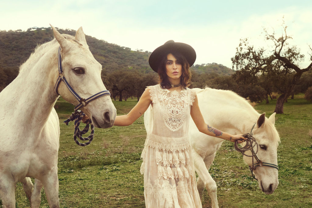 Model in white dress and black hat leads two white horses for Jan/Feb ’24 Issue cover