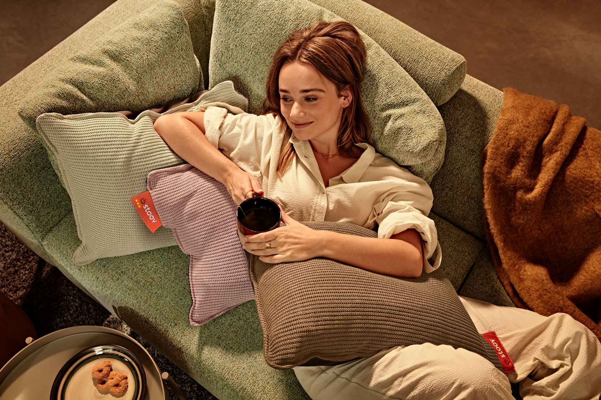 Woman reclining on sofa cushions, holding a mug.