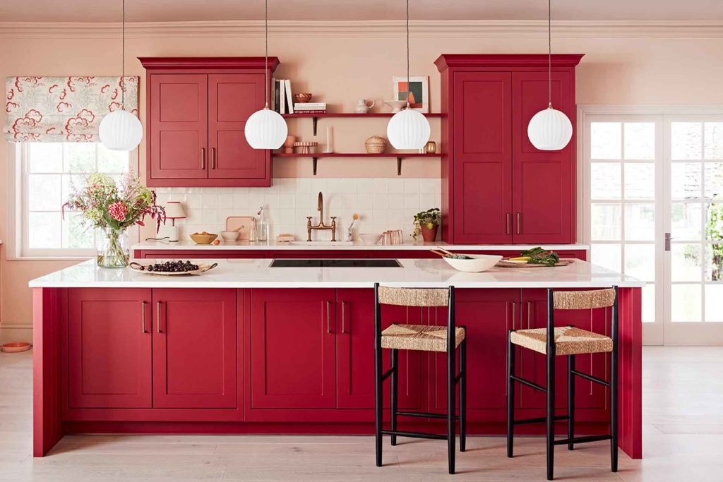 Red kitchen cabinets and island with white countertops.