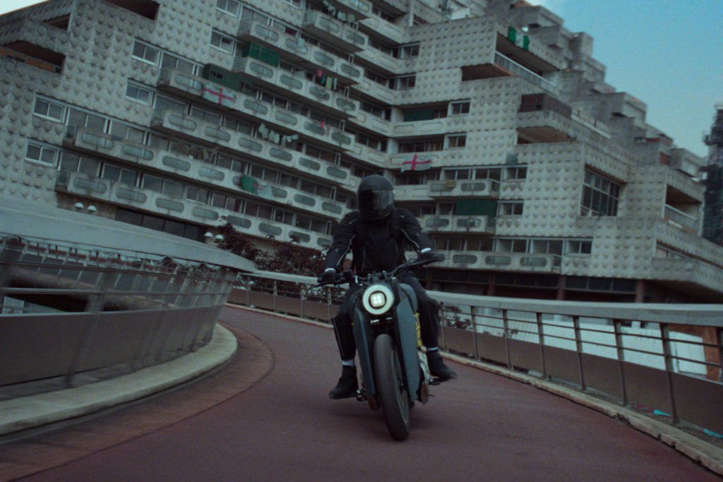 A man on a motorbike driving away from a housing block