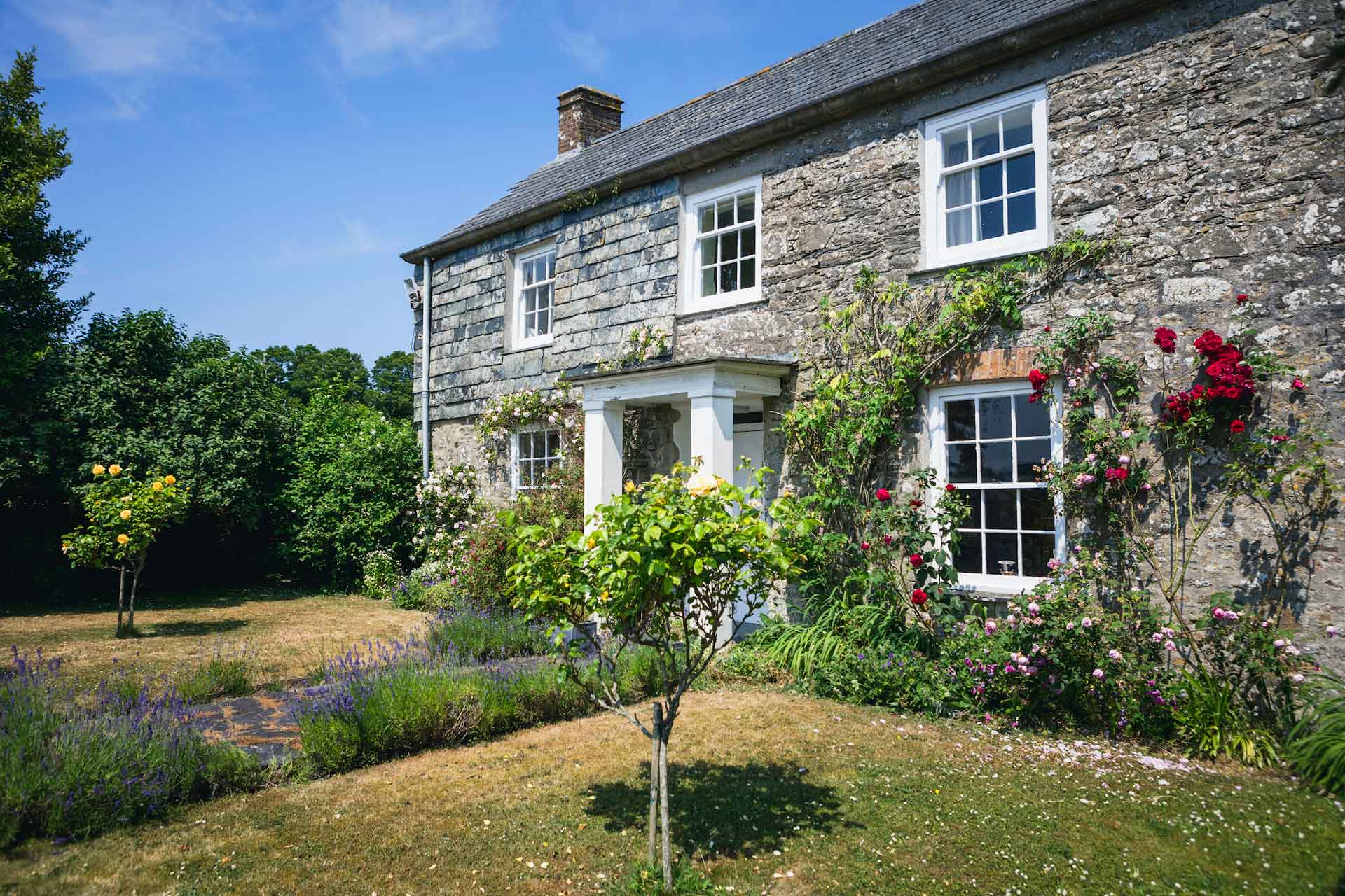 Stone cottage with shrubs and flowers in front.