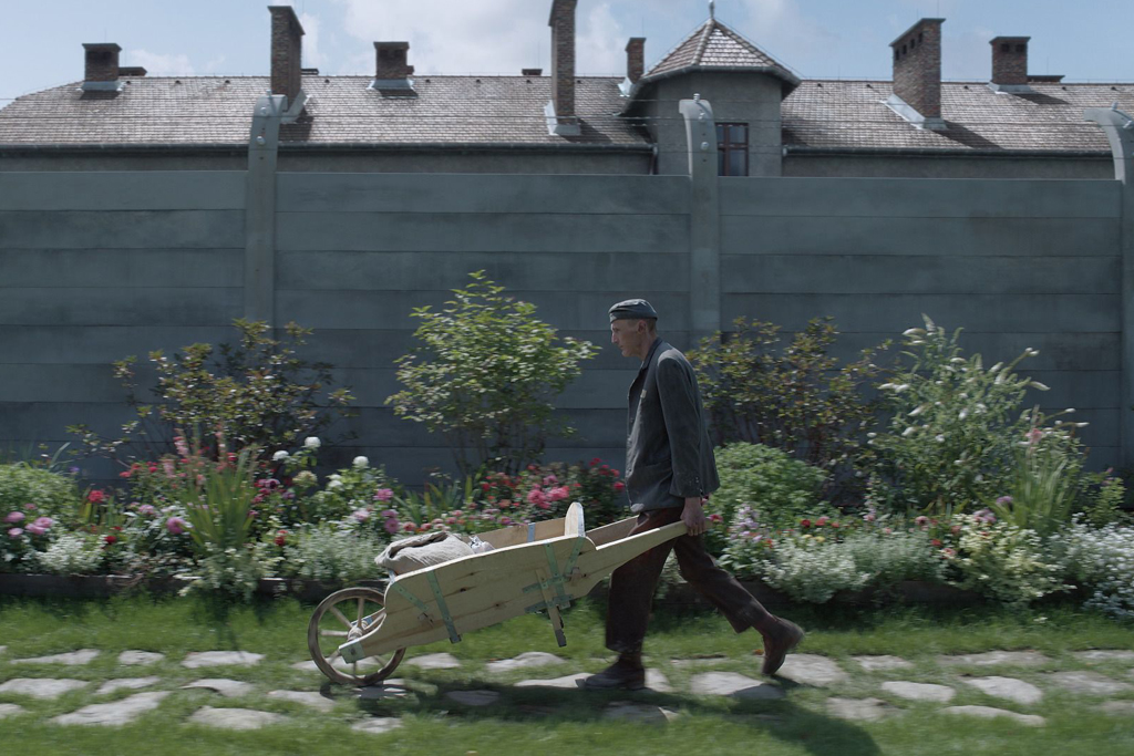 A man walking a wheelbarrow beside some plants