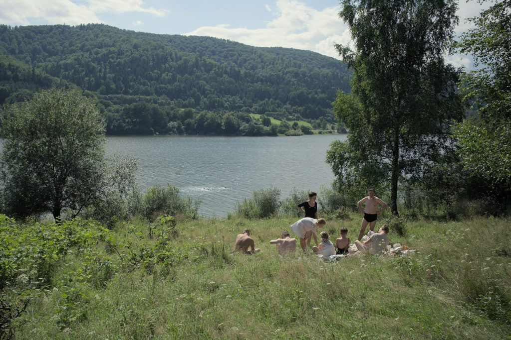 A still from The Zone of Interest depicting a family in a meadow beside a lake