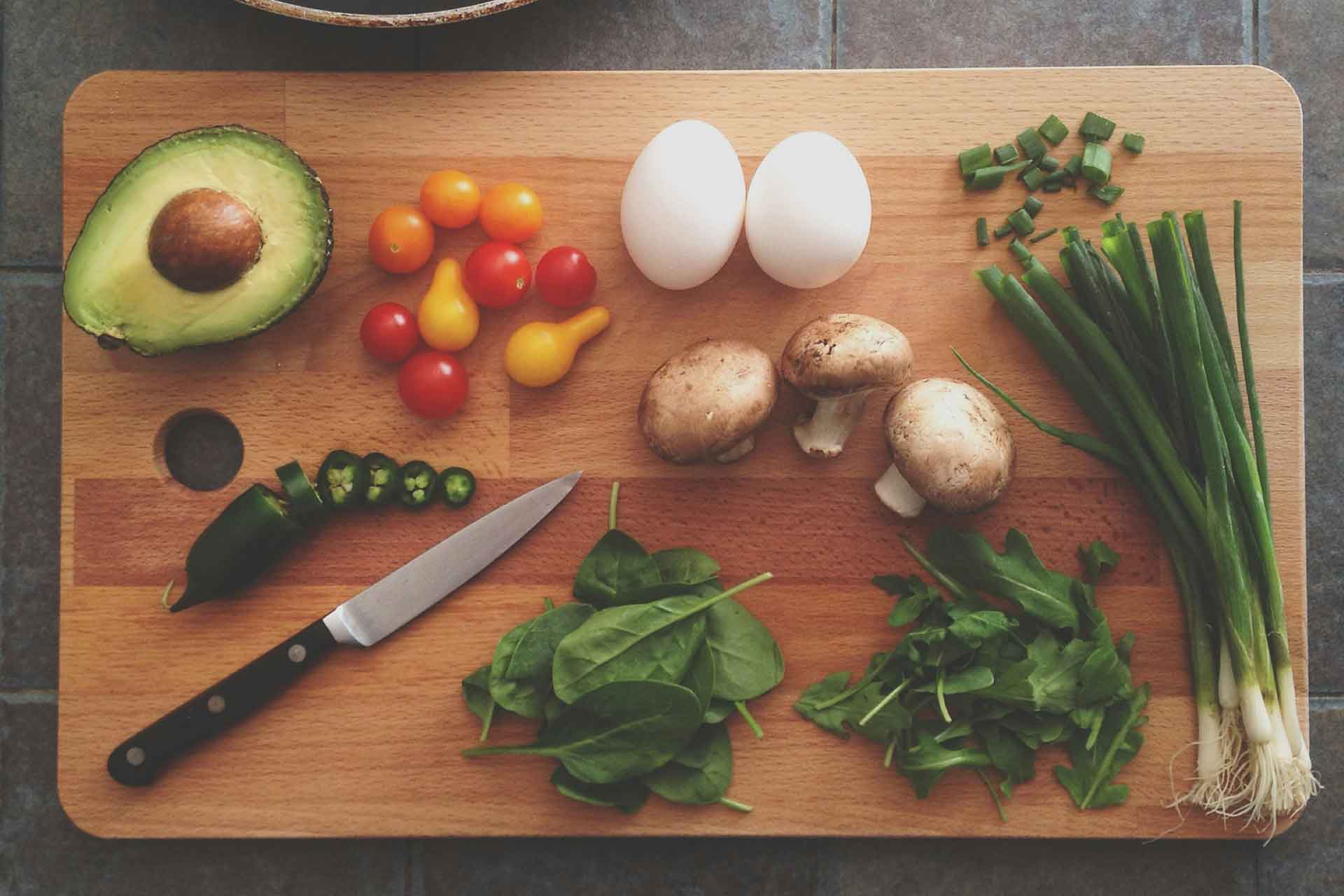 Aerial view of chopping board with avocados, spring onions, eggs and a knife.