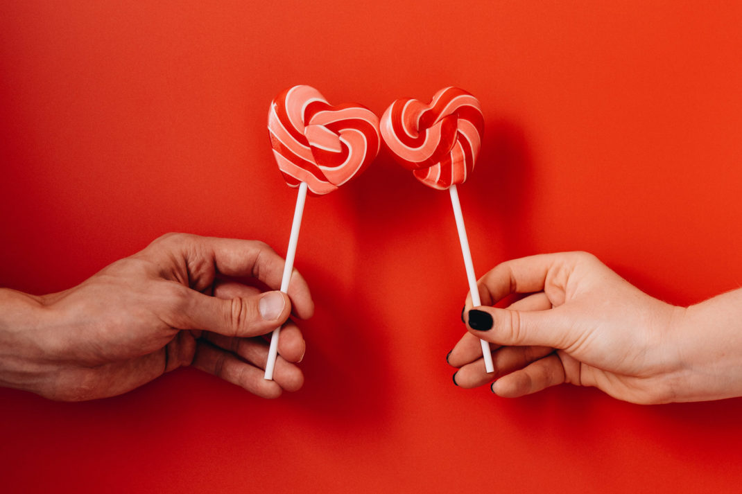 Two people holding Valentine's Day heart shaped lollipops