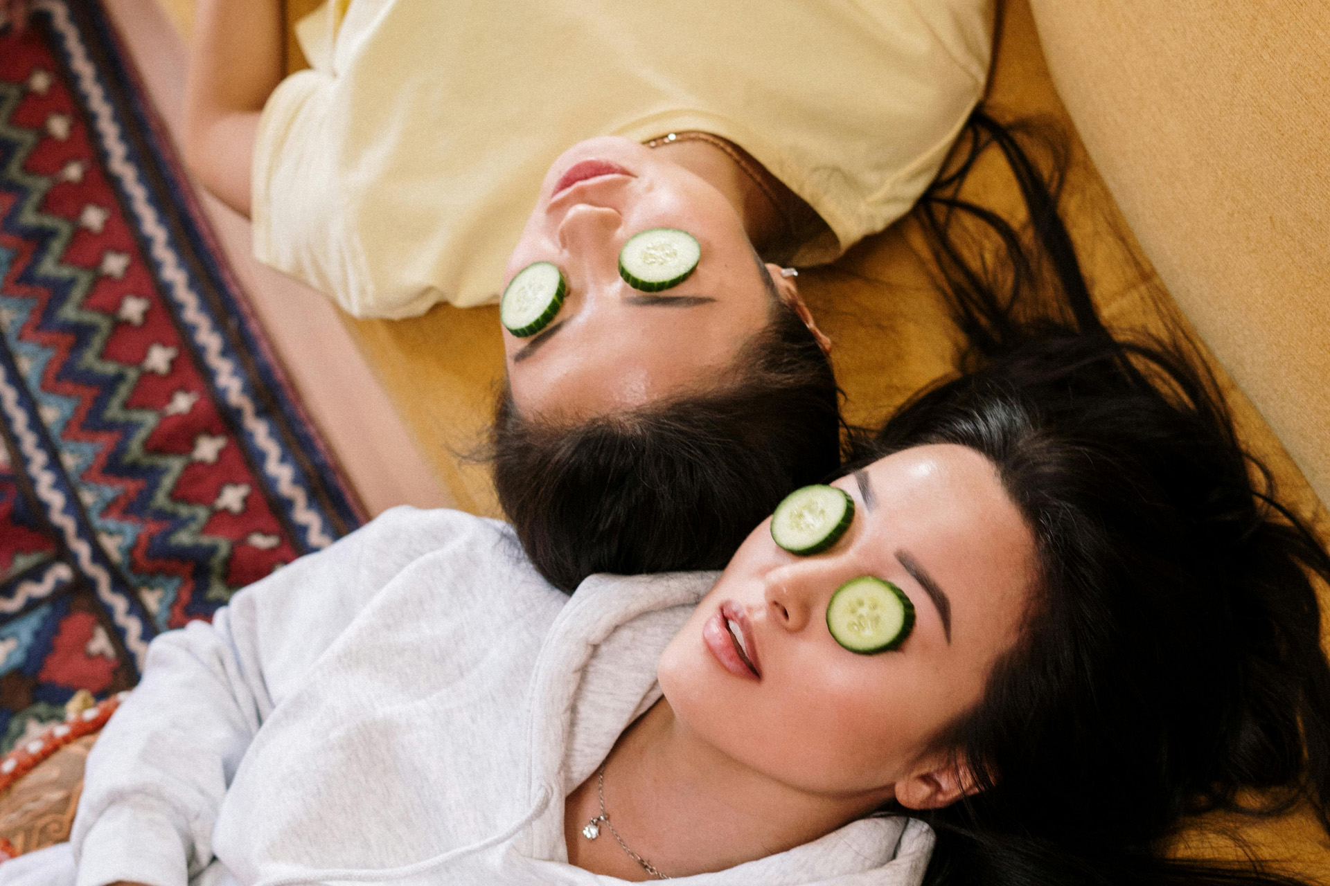 Two people at home with cucumber slices over their eyes