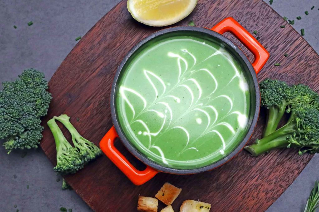 Bowl of green soup with broccoli florets and croutons