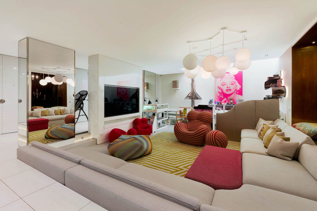 Large living room with cream sofas, red accents and a red armchair.
