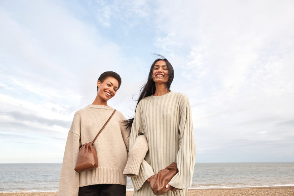 Two women in knit jumpers smiling while on beach