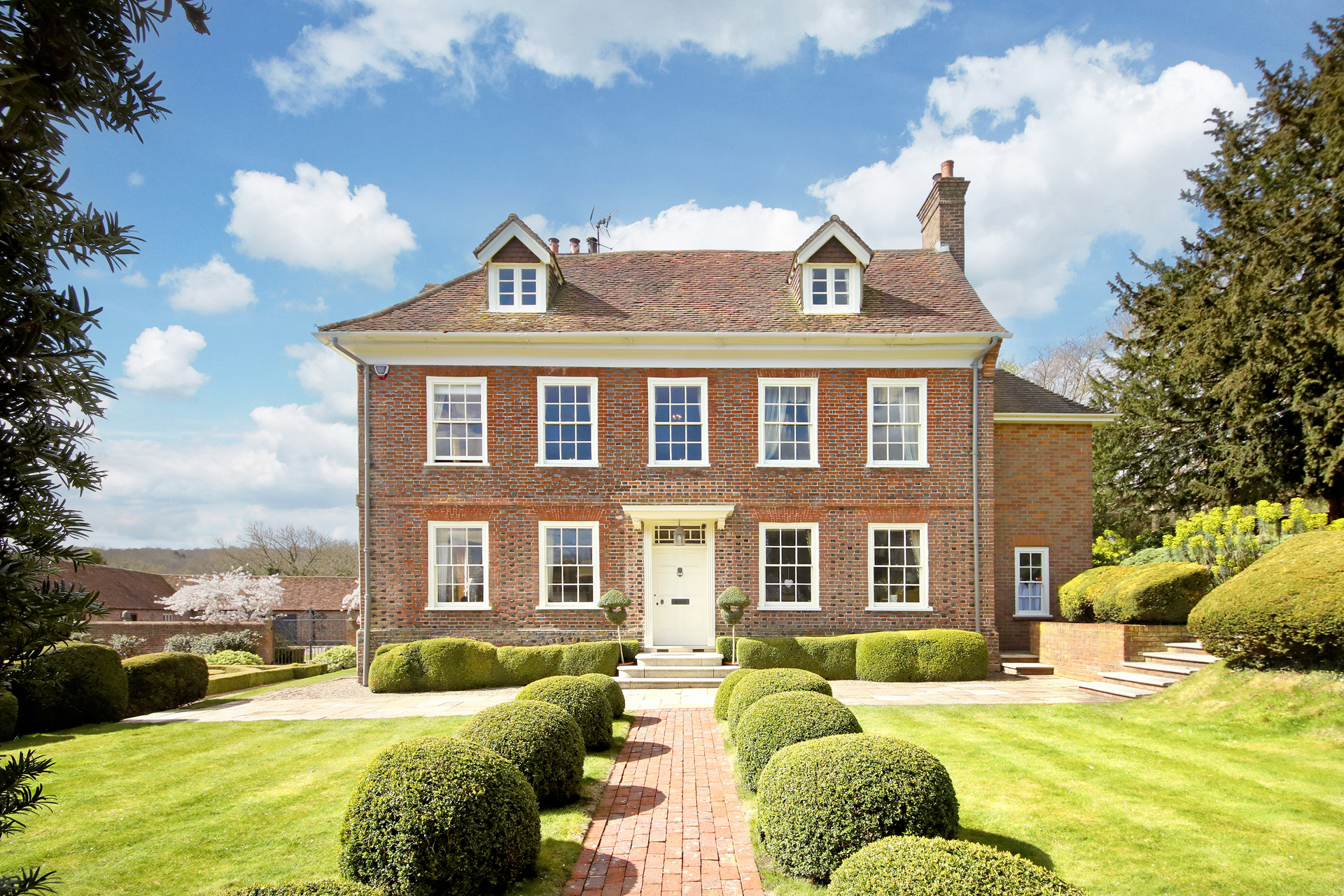 Red brick country manor with a hedge-lined path leading to the door.
