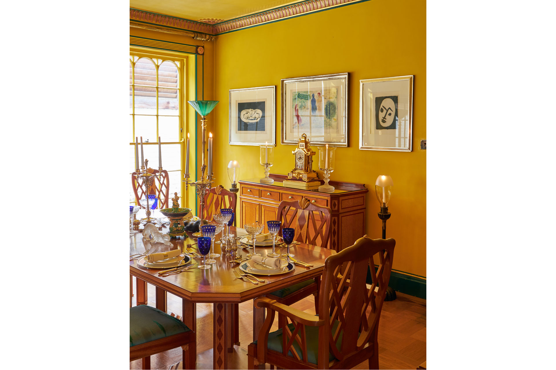 Sunflower=yellow dining room with polished wooden furniture and intricate ceiling cornicing.