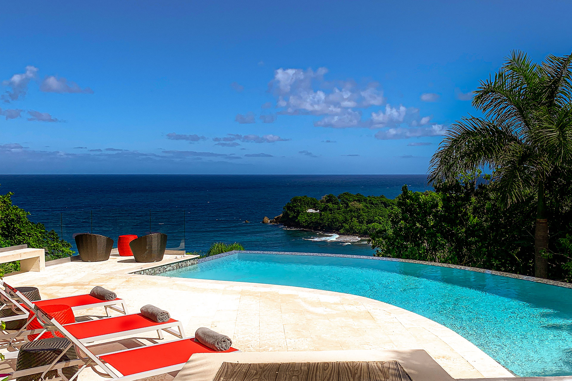 Infinity pool with red sun loungers and a view of the ocean.
