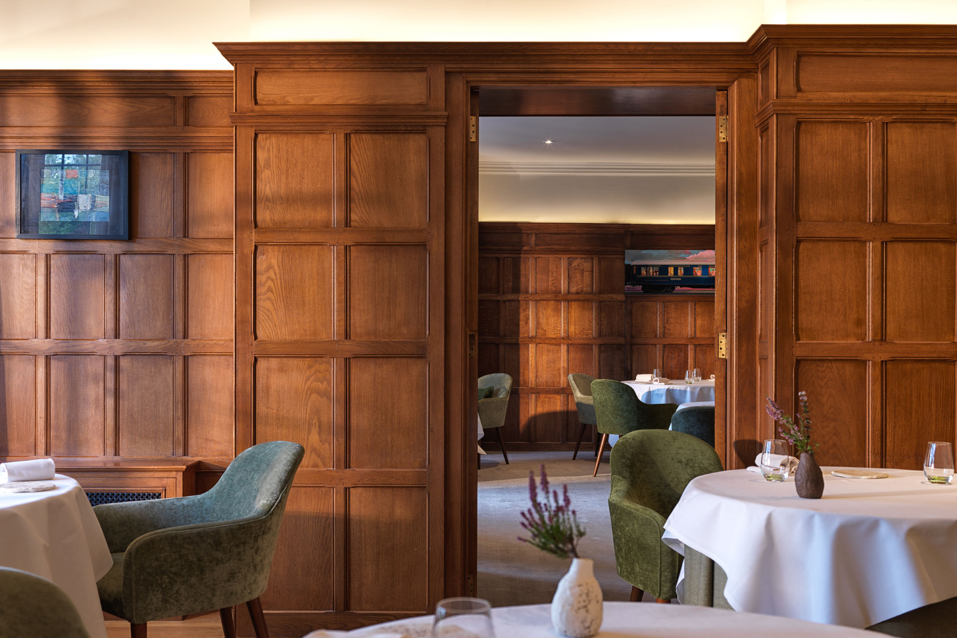 Wood-panelled dining room with white tablecloths and circular tables.