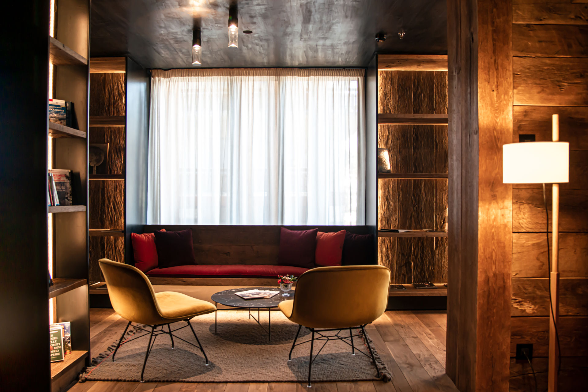 Reception area with red sofas, wooden bookshelves and white curtains.