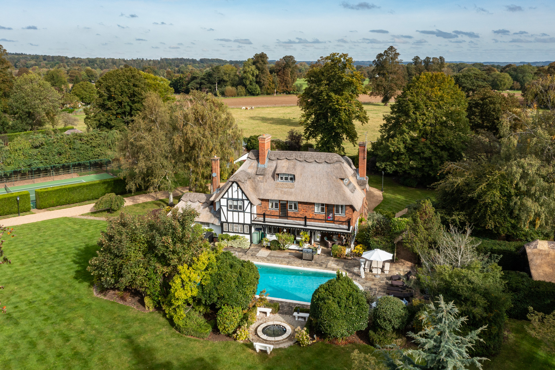 Thatched, timber-framed home with outdoor swimming pool and lawns surrounding it.