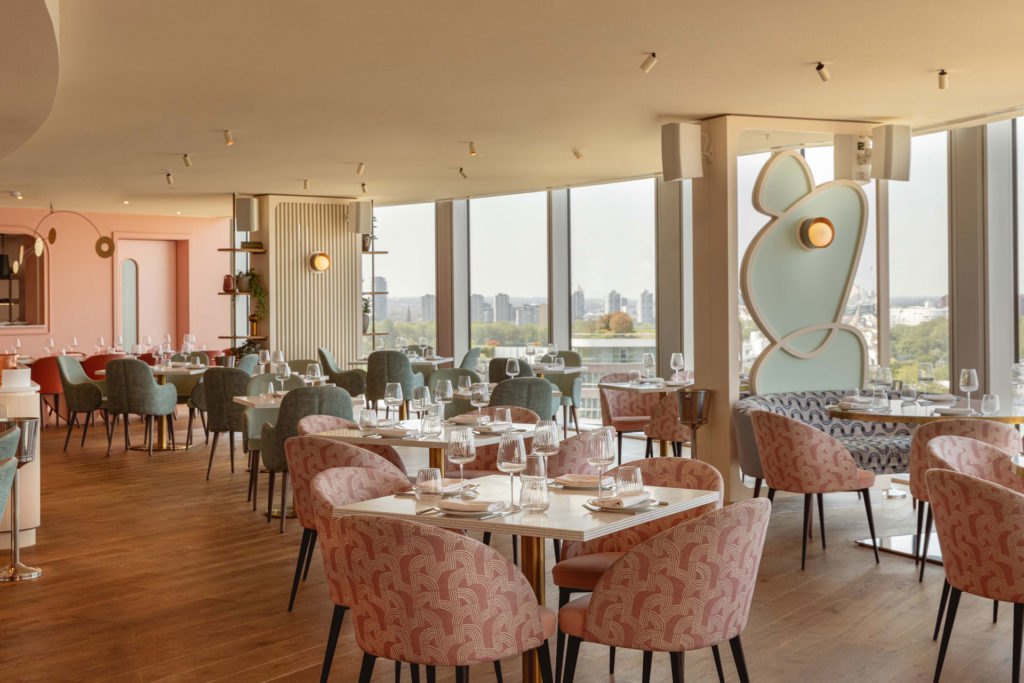 JOIA interiors, with floor-to-ceiling windows, pink chairs and curved mirrors.