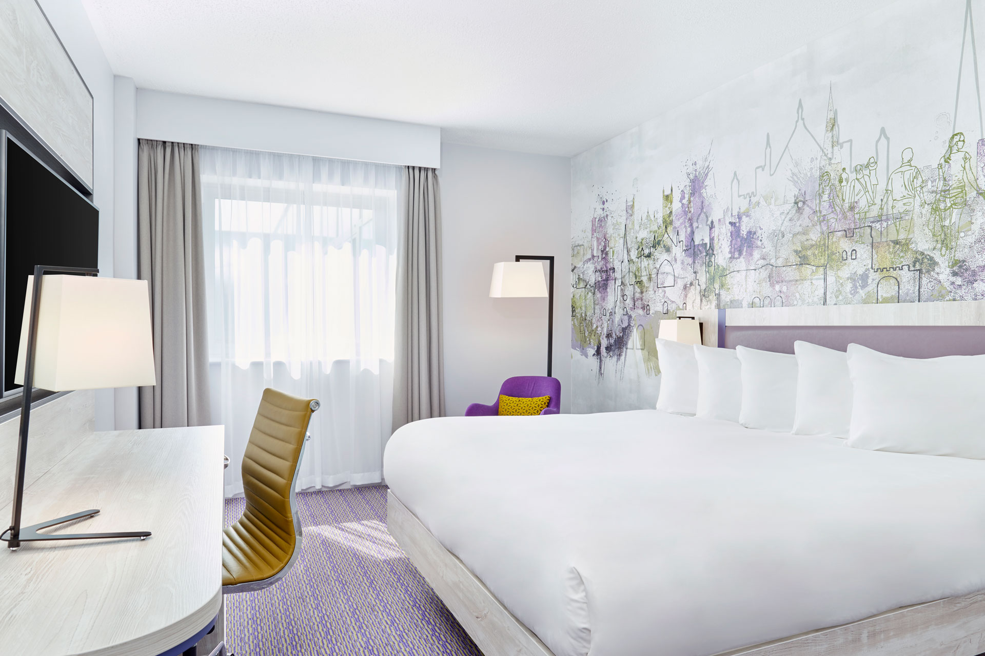 Hotel bedroom with white sheets, a mustard yellow desk chair and lilac accents