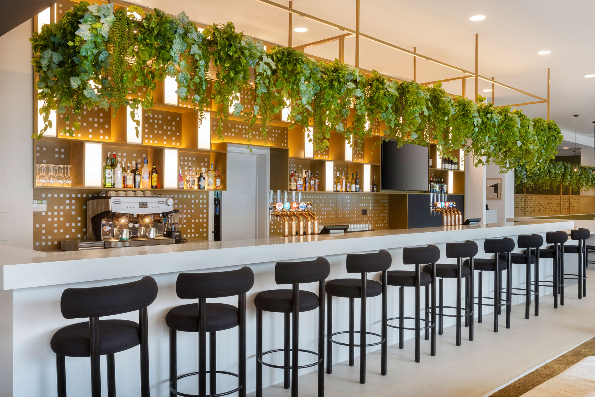 Bar with black bar stools, gold accents and faux plants hanging from the ceiling