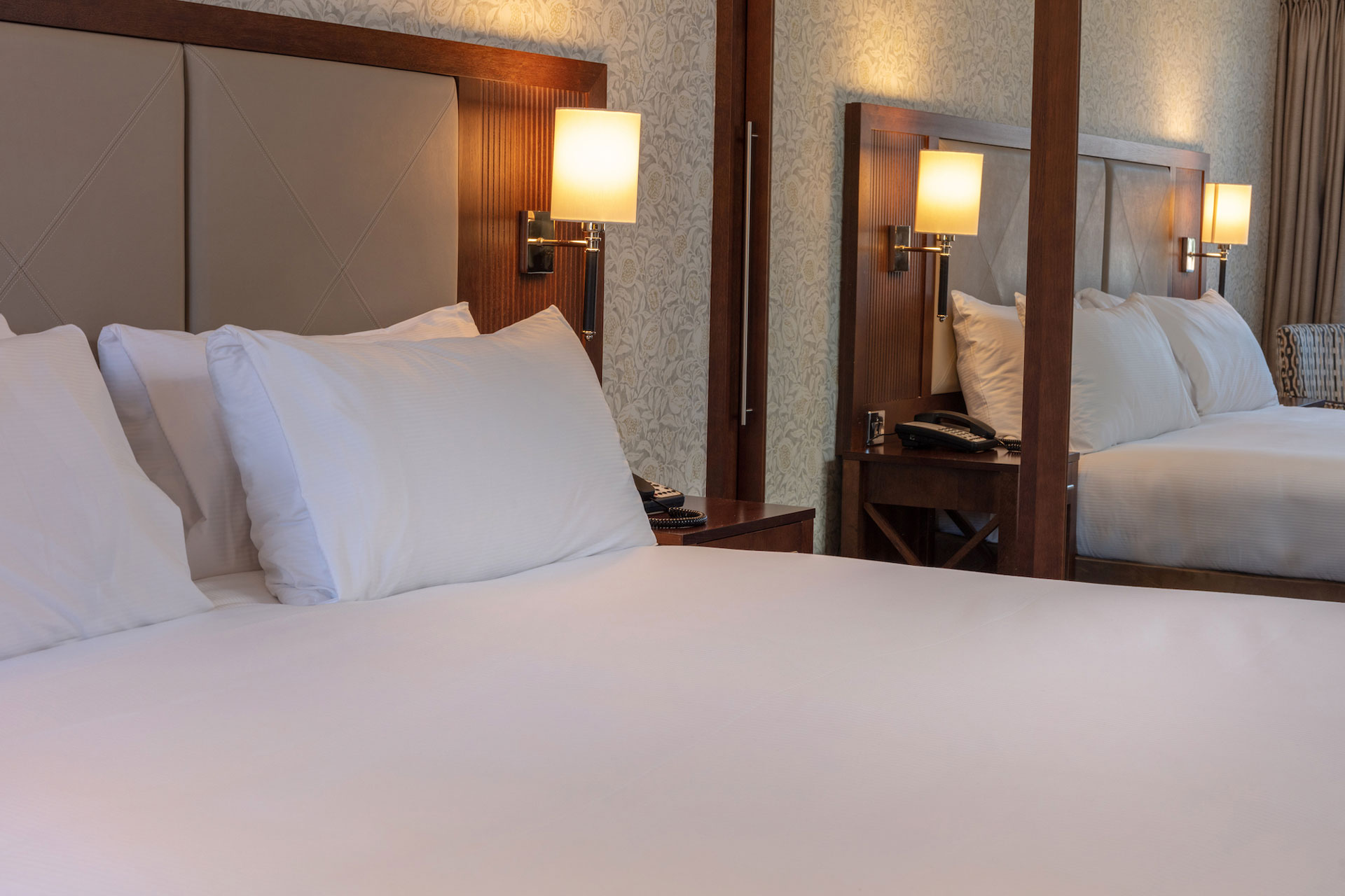 Bedroom with white sheets and a mirrored wardrobe.