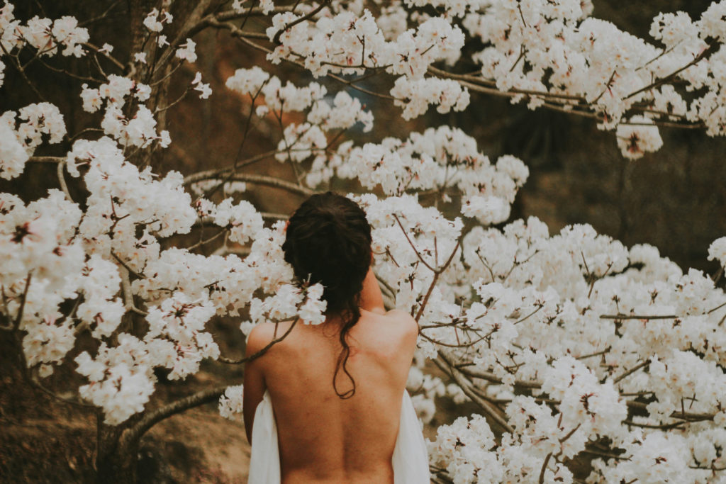 Woman stood amongst flowering trees with bare back | beauty ingredients to avoid