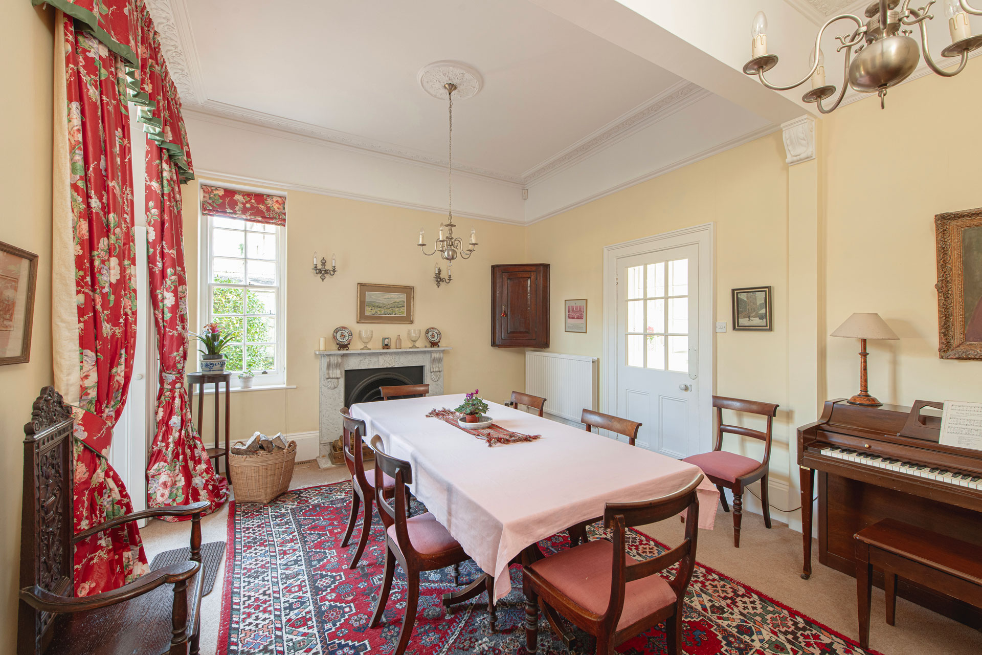 Dining room with wooden chairs, white tablecloth and red curtains.