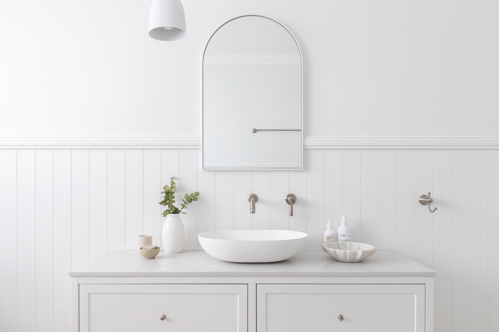 White bathroom with arched mirror and silver accents