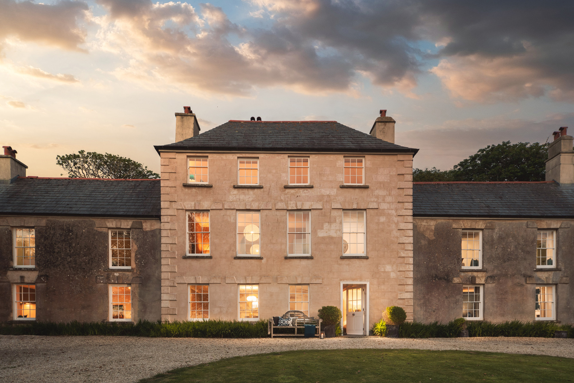 Large country manor with gravel driveway, photographed at dusk.