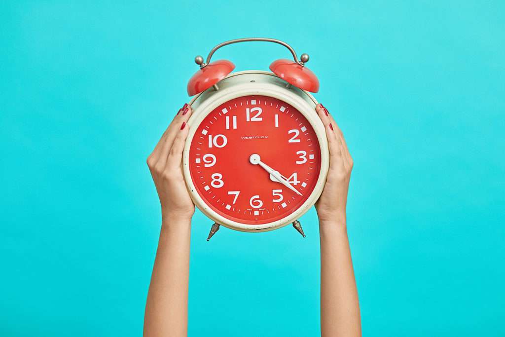 Hands holding up a red clock against a blue background