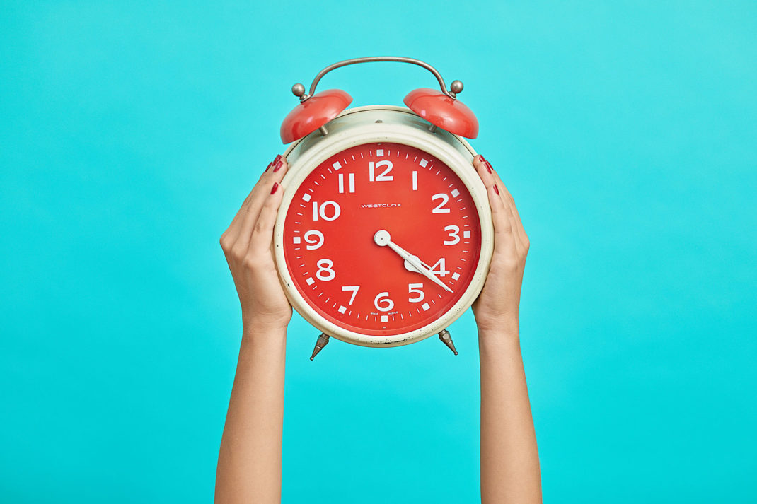 Hands holding up a red clock against a blue background