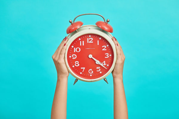 Hands holding up a red clock against a blue background