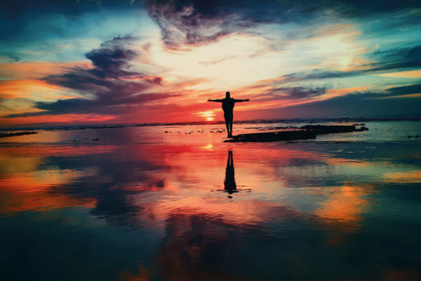 A figure on the beach embracing the colourful sky