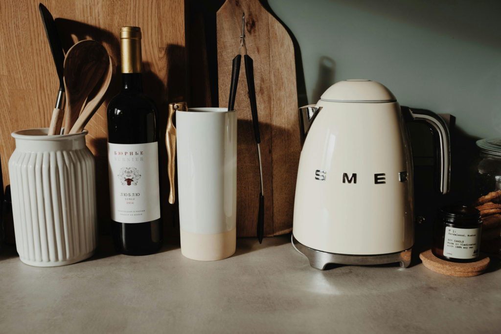 White SMEG kettle with black handle, on a kitchen countertop with white utensil pots.