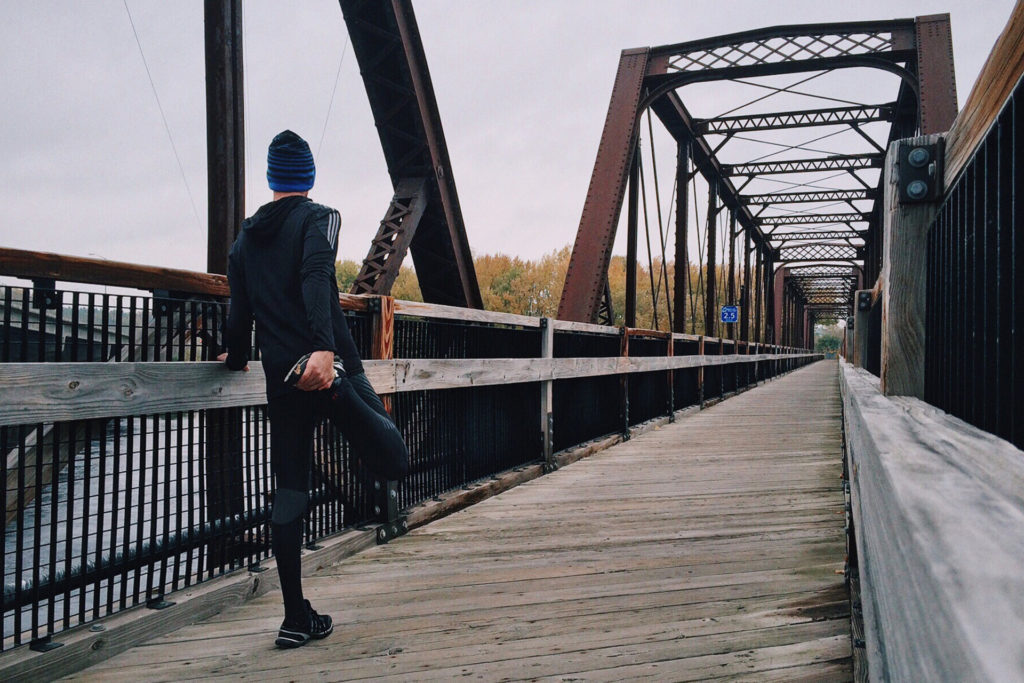 A man stretching before he begins a run along a bridge