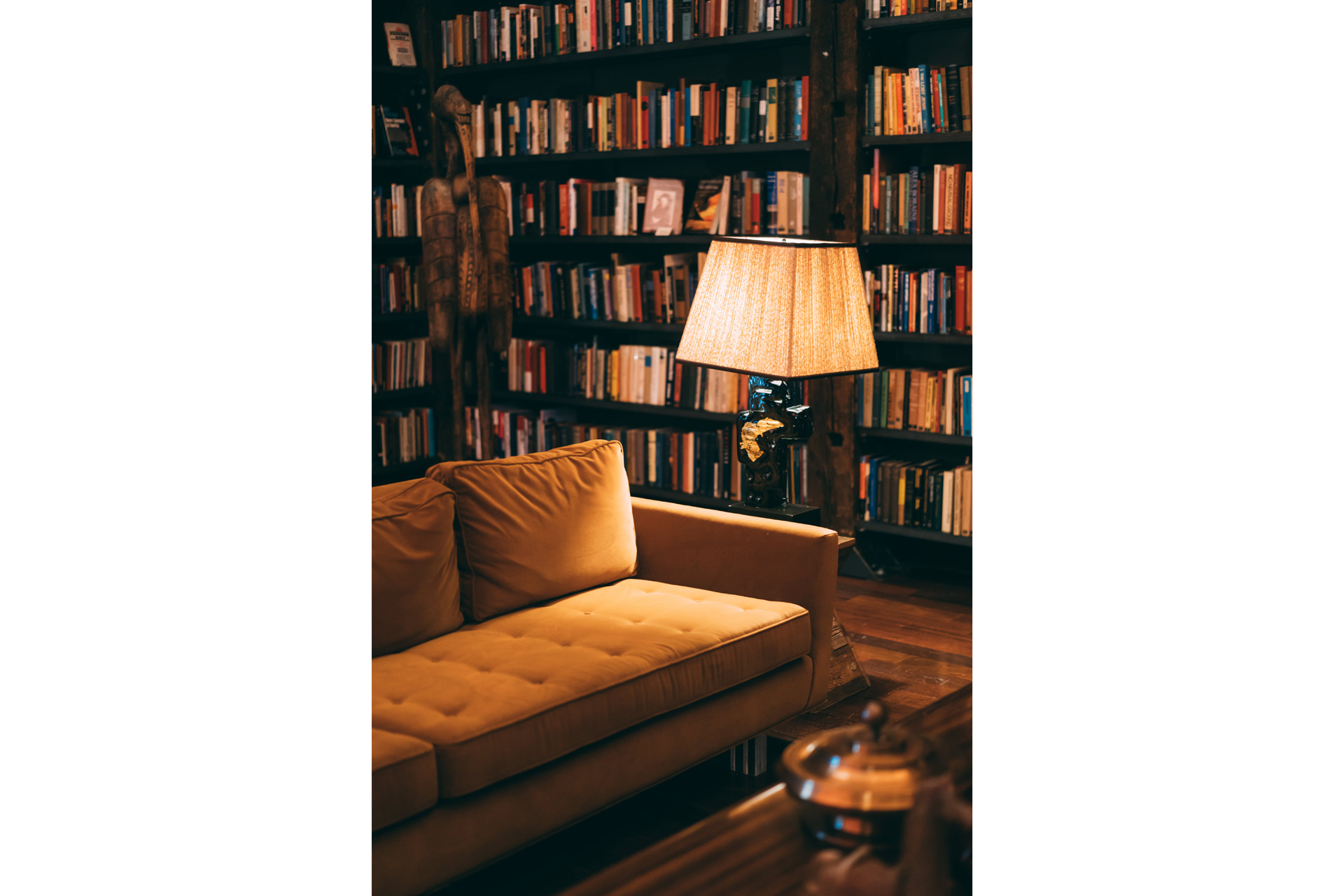 A cosy room with a sofa, lampshade and large bookshelf