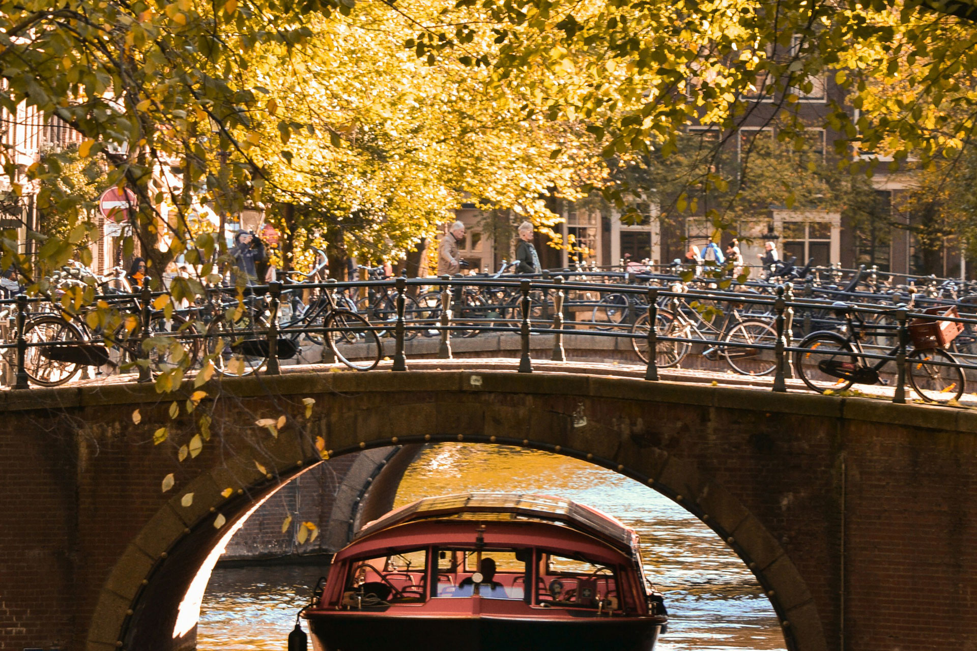 Bridge in Amsterdam with cyclists riding along it and a boat passing underneath.