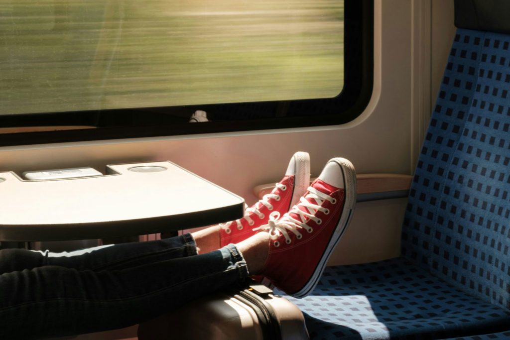 Pair of legs wearing red Converse trainers and resting on top of a suitcase on a train.