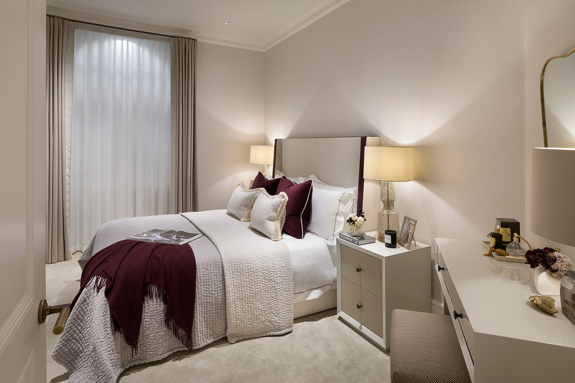 Modern bedroom with white linens, a dark red throw blanket and taupe curtains.