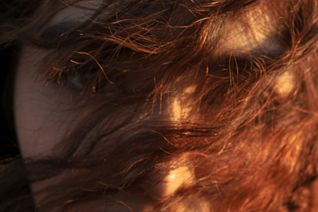 Close up of woman's face with copper cowboy hair over face
