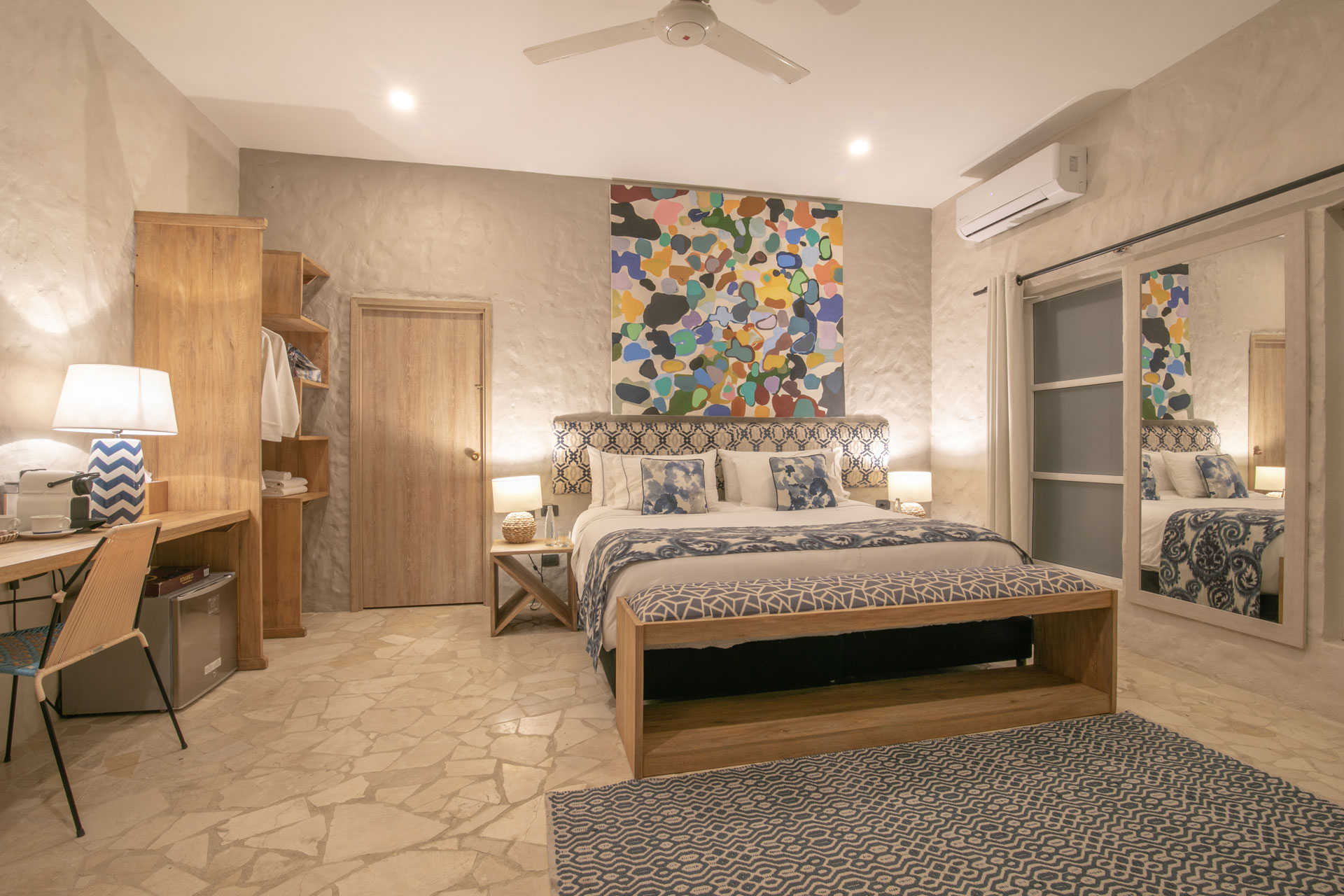 Hotel bedroom with grey accents, wooden furniture and a colourful abstract mural above the bed.